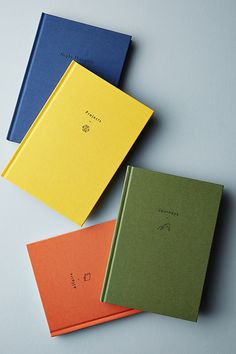 four different colored notebooks sitting next to each other on top of a white surface