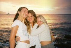 three girls are hugging on the beach at sunset