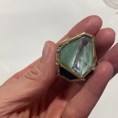 a person holding a ring with a green stone in it's middle and gold trimmings around the edges