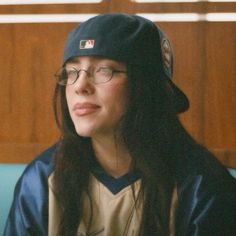 a woman with long hair wearing a baseball cap and glasses sitting in a blue chair