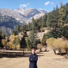 a man standing in the middle of a field with trees and mountains in the background