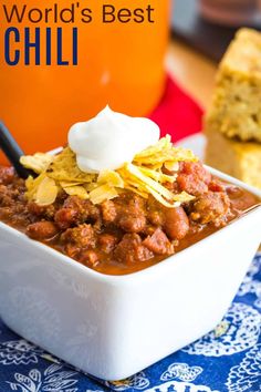 chili in a white bowl with sour cream on top and cornbreads next to it