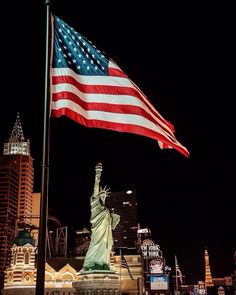 the statue of liberty is lit up at night in new york city, with skyscrapers behind it