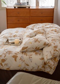 a bed with a flowered comforter on top of it next to a dresser