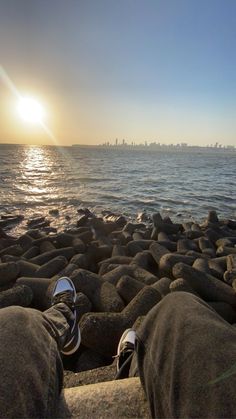 someone's feet are on the rocks near the water as the sun is setting