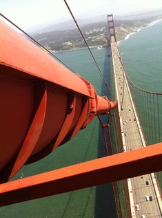 an orange pipe is on the side of a bridge over water and cars are driving down it