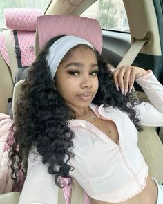 a woman sitting in the back seat of a car wearing a pink headband and white shirt