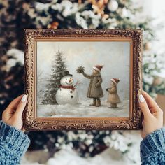 a person holding up a painting with a snowman and two dogs in front of a christmas tree