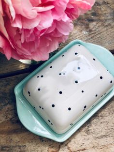 a white and blue plate with black dots on it next to a pink peonie