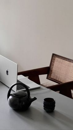 an apple laptop computer sitting on top of a white table next to a teapot