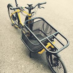 a yellow bicycle with a basket on the front and rear wheels is parked in a parking lot