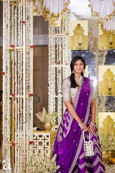 a woman in a purple and white outfit standing next to a wall with beads on it