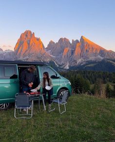 two people sitting at a table in front of a van with mountains in the background