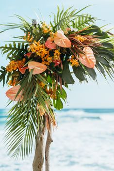 an arrangement of tropical flowers and palm leaves on a tree at the beach in front of the ocean