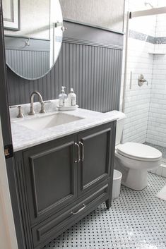 a white toilet sitting next to a gray sink in a bathroom under a large mirror