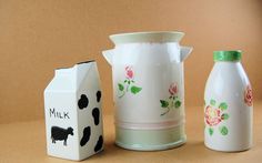 three milk jugs, one painted with flowers and the other decorated with a cow