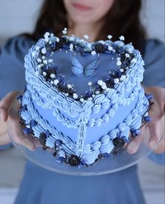 a woman holding a heart shaped cake with blue frosting and white flowers on it