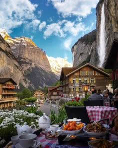 a table with food on it in front of a mountain village and some mountains behind it