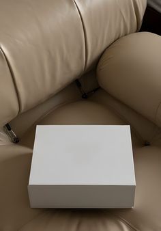 a white box sitting on top of a brown leather couch next to a pillow and arm rest