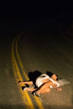 a woman laying on the side of a road at night