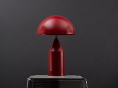 a red table lamp sitting on top of a metal box next to a black wall