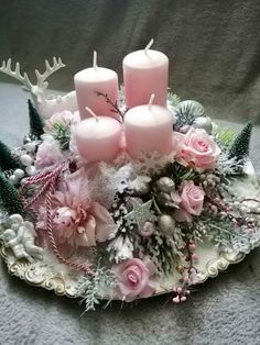 some pink candles are sitting in a tray with flowers and greenery on it's side