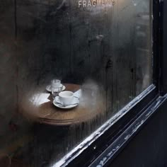 two cups and saucers sit on a wooden table in front of a dirty window