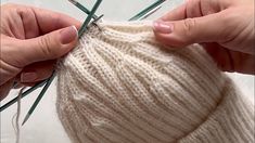 two hands holding green needles over a white knitted bag that is being sewn