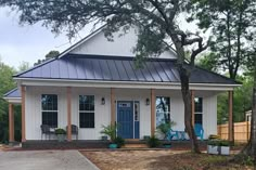 a white house with a blue door and porch in the front yard is surrounded by trees