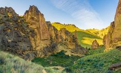 the mountains are covered with green grass and yellow rocks in the foreground is a dirt path