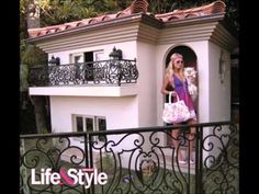 a woman holding a dog in her hand and standing next to a house with wrought iron railings