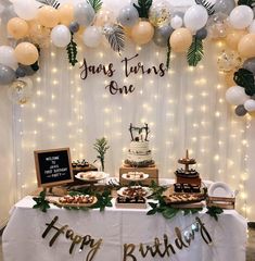 a table topped with cake and desserts next to a white wall covered in balloons