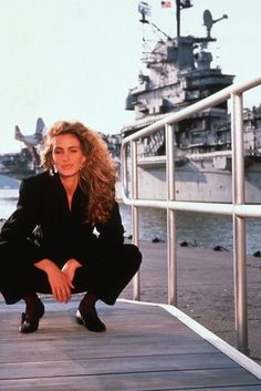 a woman sitting on a dock next to a large ship