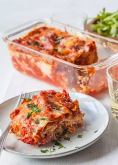 a white plate topped with lasagna next to a glass of wine and salad