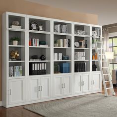 a living room with white bookcases and ladder