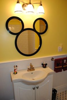 a bathroom sink with mickey mouse mirror above it and other decorations on the wall behind it