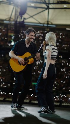 a man holding a guitar while standing next to a woman with a microphone in her hand