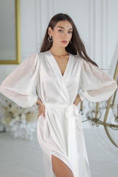 a woman wearing a white robe with sheer sleeves and thigh high slits standing in front of a mirror