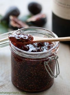 a jar filled with jam next to a bottle of wine and wooden spoons on a table