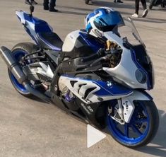 a blue and white motorcycle parked on top of a parking lot next to other people