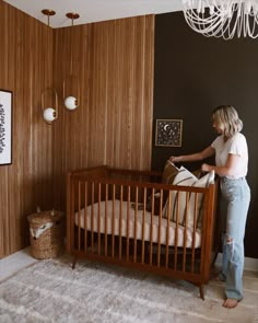 a woman standing next to a baby crib in a room with wood paneling