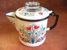 a white tea pot with colorful designs on the lid and black handle, sitting on a brown surface