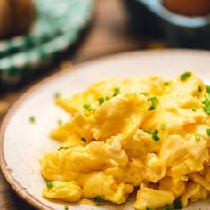 scrambled eggs on a plate with chives and an egg in the backgroud