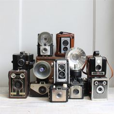 an assortment of old cameras sitting on top of each other in front of a white wall