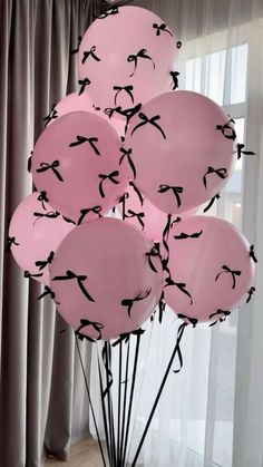 a bunch of pink balloons with black birds on them in front of a curtained window