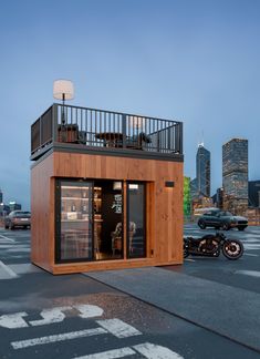 a small wooden building sitting in the middle of a parking lot next to a motorcycle