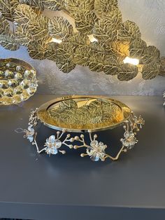 two gold and silver plates sitting on top of a table next to another plate with flowers