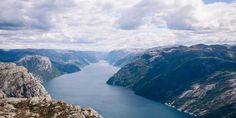 a lake surrounded by mountains under a cloudy blue sky with white clouds in the distance