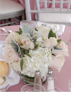 a vase filled with white and pink flowers on top of a table next to wine glasses