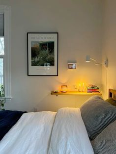 a bed with white sheets and pillows next to a night stand on the wall above it